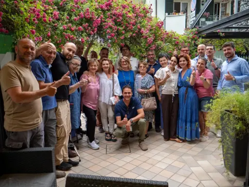 Un gruppo di persone sorridenti festeggia la primavera viserba sotto un pergolato fiorito.