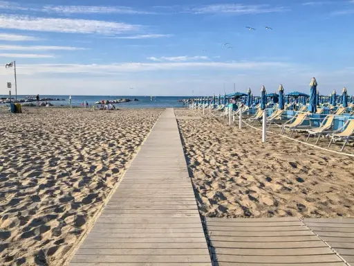 Passerella in legno sulla sabbia dorata di Rimini, con file di lettini e ombrelloni blu pronti per accogliere i bagnanti.