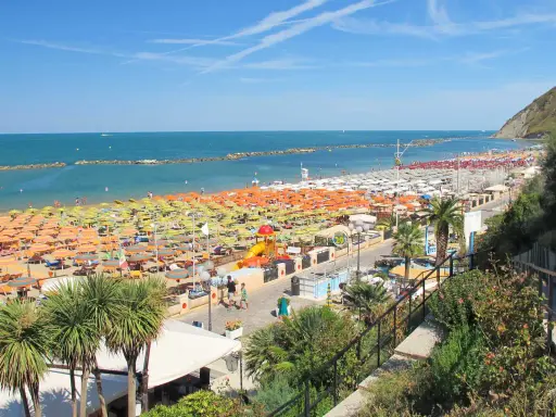 Ampia spiaggia libera a Gabicce Mare, con file infinite di ombrelloni colorati e lettini sotto un cielo azzurro.