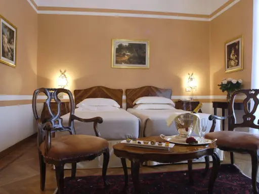 Camera elegante con due letti singoli, un tavolino con champagne e pasticcini, e sedie d'epoca. Un assaggio di lusso al Grand Hotel Rimini.