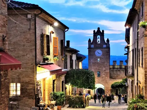 Borgo medievale illuminato al crepuscolo, con torre dell'orologio e vicoli suggestivi. Perfetto per scoprire cosa vedere vicino a Gradara.