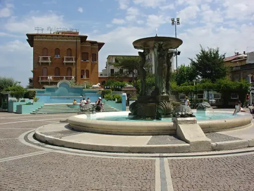 Fontana delle Sirene a Cattolica, con statue di sirene e tartarughe, circondata da edifici storici e una piazza acciottolata.