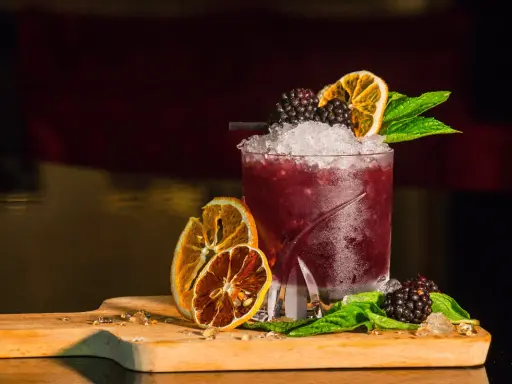 Cocktail rosso con frutti di bosco, arancia essiccata e menta, perfetto per un aperitivo a Riccione.