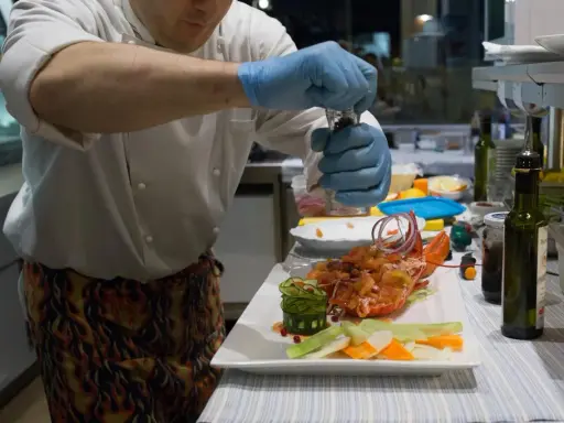 Chef con guanti blu macina pepe su un'aragosta, un piatto che sembra uscito da "lo zodiaco Rimini".