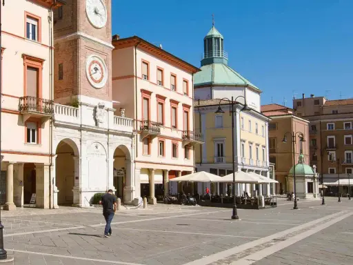 Passeggiata nella soleggiata piazza Tre Martiri a Rimini, con i suoi palazzi storici e il caratteristico orologio.