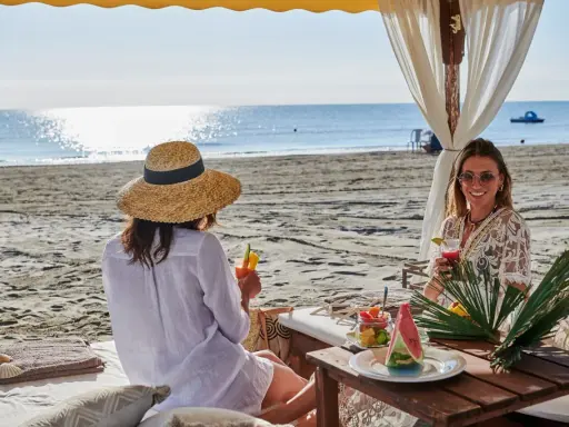 Due donne sorseggiano cocktail in un bagno Jacarè a Cervia, godendosi la spiaggia e il mare.