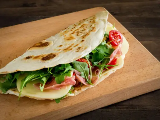 Piadina romagnola, un classico dal sapore autentico, ripiena di prosciutto, formaggio, rucola e pomodorini.