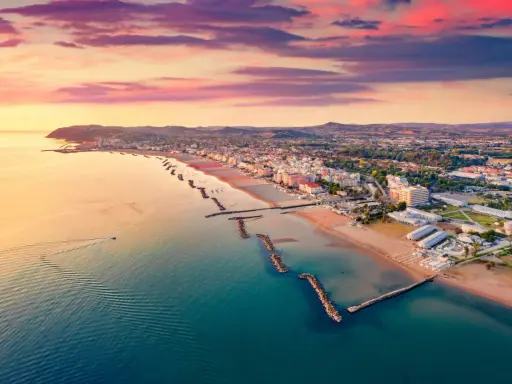 Alba rosata sul porto di Cattolica, con la costa e le spiagge dorate che si estendono verso l'orizzonte.