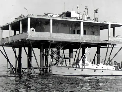 La struttura su palafitte, nota come Isola delle Rose, ospita persone su una barca ormeggiata.