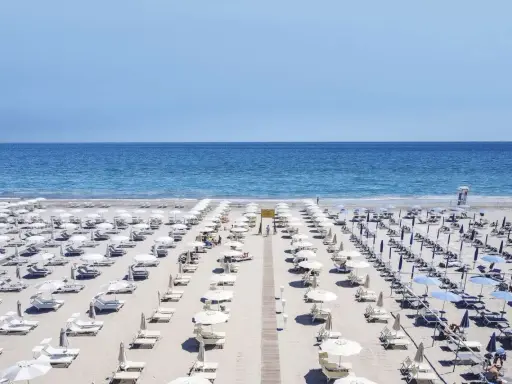 File di ombrelloni bianchi e lettini ordinati sui **stabilimenti balneari Cervia**, con il mare azzurro sullo sfondo.