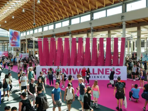 Folla animata a Rimini Wellness, un evento dedicato al benessere e al fitness. Persone di ogni età passeggiano tra gli stand e le aree espositive.
