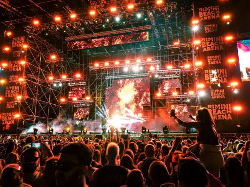 Folla in delirio al Rimini Beach Arena, luci psichedeliche e musica pulsante per un evento indimenticabile.