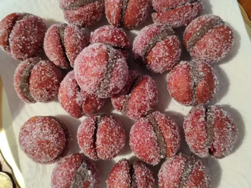 Dolci castagnole romagnole, due semisfere rosse unite da una crema scura e ricoperte di zucchero.