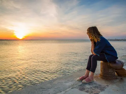 Donna seduta osserva il tramonto a Rimini, con il sole che si riflette sul mare calmo.