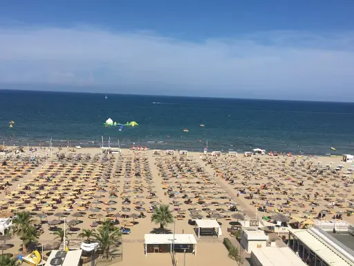 Una vasta spiaggia di Miramare gremita di ombrelloni e lettini, con bagnanti che si godono il sole e il mare azzurro.