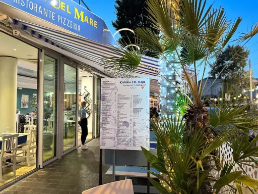Osteria del Mare, ristorante pizzeria a Rimini centro, con menù esposto e tavoli all'esterno. Palme illuminate con lucine.