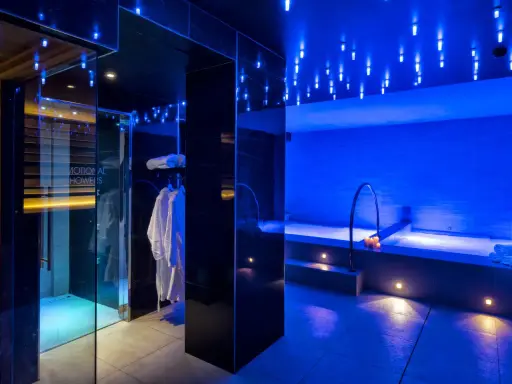 Interni di un centro benessere a Riccione con docce emozionali, vasca idromassaggio e accappatoi bianchi, illuminati da luci blu soffuse.