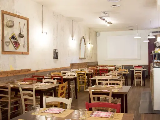 Interno di un ristorante accogliente, con tavoli apparecchiati e sedie colorate. Sembra proprio il posto ideale per una cena da "la mi mama Rimini".