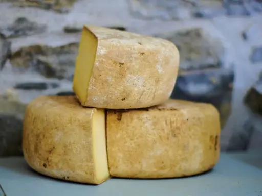 Formaggio Fossa stagionato, con crosta rustica e pasta gialla, impilato su uno sfondo di pietra grezza.