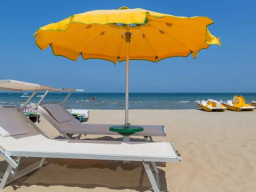 Spiagge di Rimini con lettini, ombrellone giallo e pedalò pronti per l'estate.