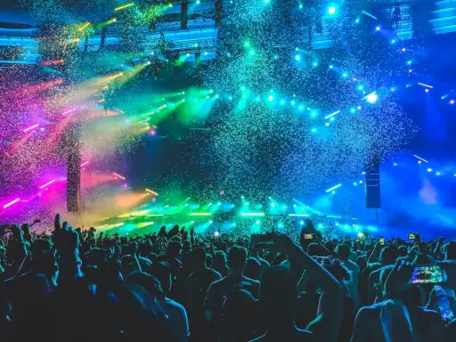 Folla in delirio a un concerto a Rimini, con coriandoli colorati e luci psichedeliche che illuminano la scena.