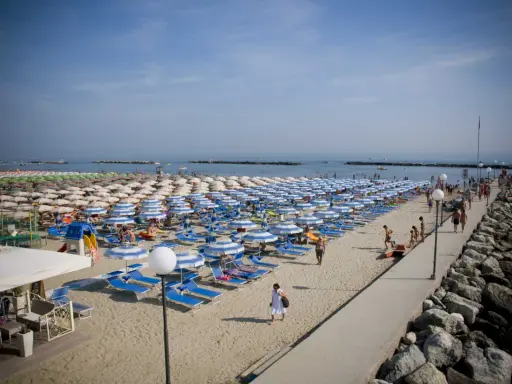 Spiaggia affollata a Gatteo Mare centro, con file di ombrelloni e lettini, gente che passeggia sul molo e si gode il sole.