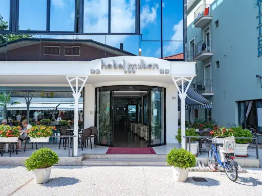 Ingresso accogliente dell'Hotel Milton Valverde con tavolini all'aperto e fiori colorati. Biciclette parcheggiate, pronte per esplorare.
