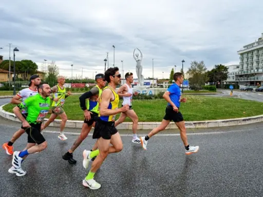 Atleti impegnati nella Rimini Half Marathon, corrono su asfalto bagnato con un cielo nuvoloso.