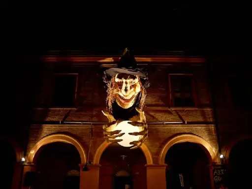 Una strega spaventosa con un cappello nero e una sfera luminosa in mano, illuminata nella notte. Sembra la protagonista de la notte delle streghe.