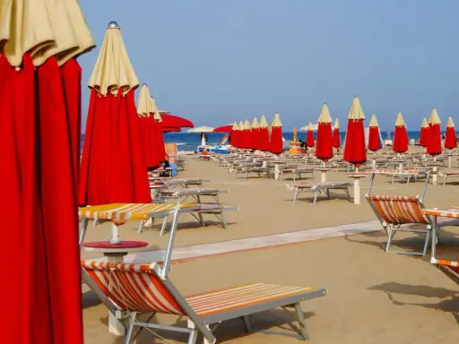 Filettate di lettini e ombrelloni rossi e gialli sulla spiaggia di Rimini Nord, pronti per accogliere i bagnanti.