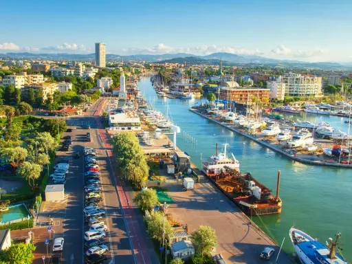 Vista aerea di un vivace **club nautico** con barche ormeggiate, edifici moderni e un faro bianco.
