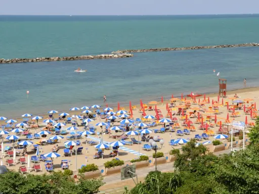 Spiaggia affollata con ombrelloni colorati, lettini e bagnanti. Perfetta idea per sapere dove andare al mare in Emilia Romagna.
