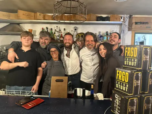 Staff sorridente a Misano Adriatico, con un ragazzo che sembra un gambero sbronzo tra loro. Sul bancone, bottiglie e lattine di "FRGD Irish Stout".