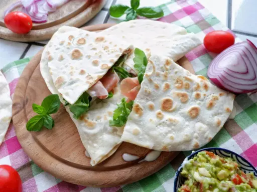 Piadina, piatto tipico di Rimini, farcita con prosciutto e rucola, servita con guacamole e verdure fresche.