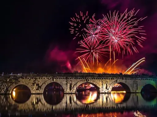 Fuochi d'artificio spettacolari illuminano il cielo notturno sopra un ponte storico, celebrando il capodanno in riviera romagnola.