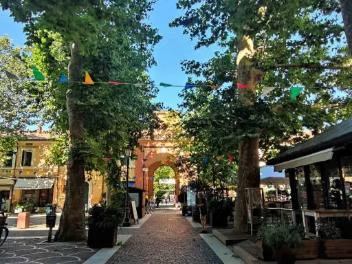 V Cervia centro, un viale alberato con festoni colorati conduce a un arco monumentale.
