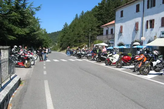 Un gruppo di motociclisti si ferma per una pausa al Passo del Muraglione, con le moto parcheggiate lungo la strada e un hotel sullo sfondo.