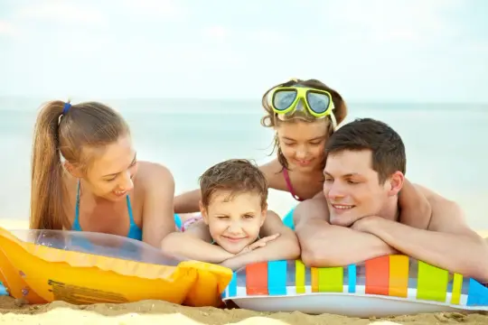 Famiglia felice in spiaggia, un'idea perfetta per Ferragosto. Bambini sorridenti e genitori rilassati su gonfiabili colorati.