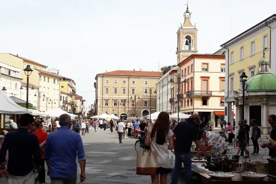 Gente passeggia tra bancarelle e palazzi storici, godendosi l'atmosfera vivace del rimini markt.