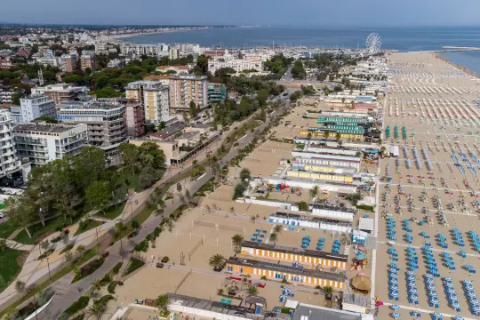 Vista aerea di una vasta spiaggia libera a Rimini, con file ordinate di ombrelloni e cabine colorate che si estendono fino al mare.