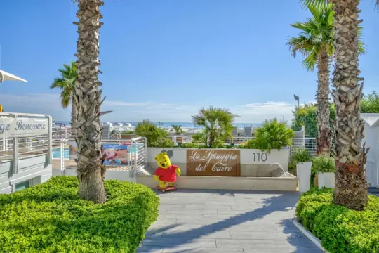Un simpatico Winnie the Pooh su skateboard accoglie i visitatori a La Spiaggia del Cuore a Riccione, con palme e il mare all'orizzonte.