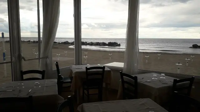 Tavoli apparecchiati in un ristorante con vista sulla spiaggia di Misano durante la bassa marea.