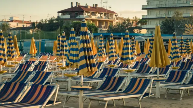 File di sdraio e ombrelloni a righe blu e gialle sulla spiaggia di Cervia Milano Marittima, pronti per accogliere i bagnanti.
