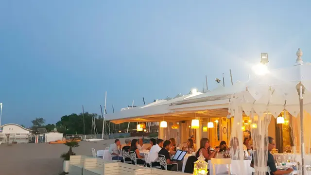 Serata in uno dei ristoranti della Riviera Romagnola, con tavoli apparecchiati sulla sabbia e luci soffuse.