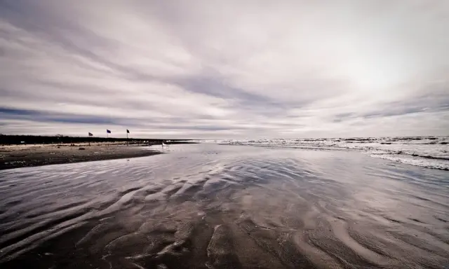 Spiaggia deserta con onde che lambiscono la riva, tre bandierine piantate nella sabbia bagnata. Un'atmosfera malinconica per questo mare d'inverno.