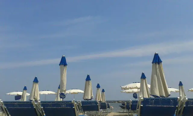 Spiaggia attrezzata al bar Lido di Savio, con lettini blu e ombrelloni bianchi e blu sotto un cielo limpido.