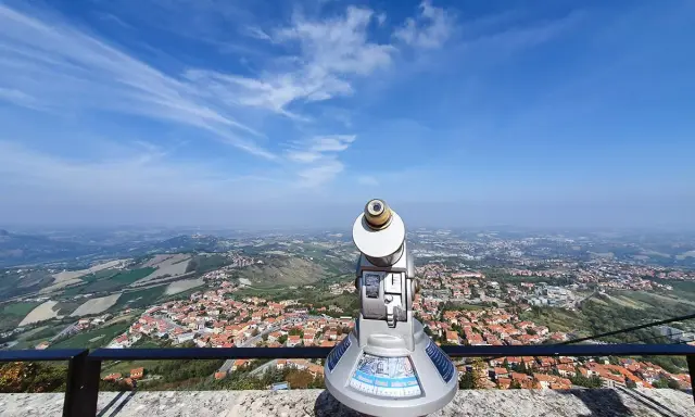 Telescopio con vista panoramica su cosa vedere a San Marino. Il paesaggio collinare e la città si estendono sotto un cielo azzurro con nuvole sottili.