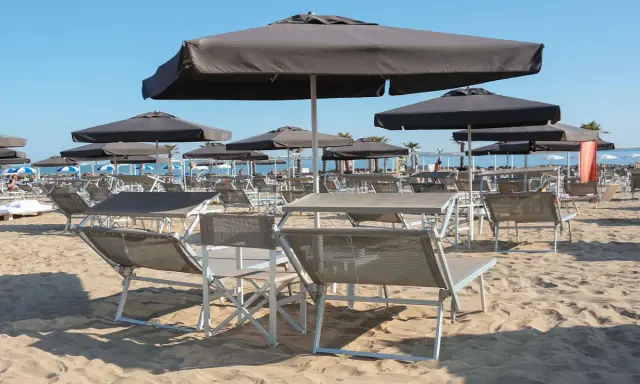 Lettini e ombrelloni scuri sulla sabbia dorata della **Baia degli Angeli Misano**, pronti per accogliere i bagnanti sotto il sole.