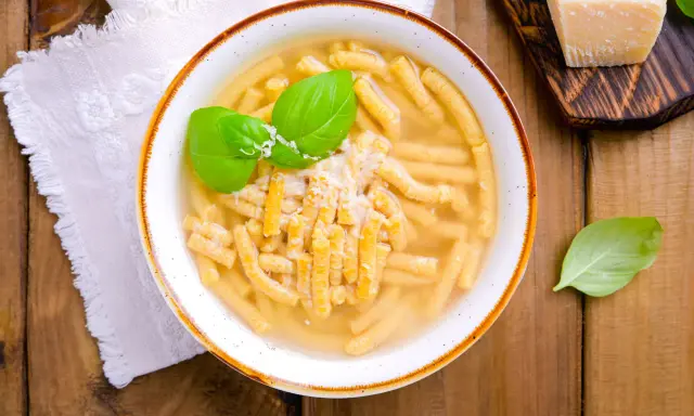 Piatto di passatelli in brodo, un classico dei piatti romagnoli, guarnito con basilico fresco e parmigiano.