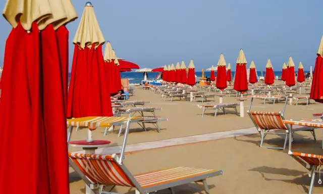 Filetto di ombrelloni rossi e lettini pronti per accogliere i bagnanti sulla costa di Rimini.